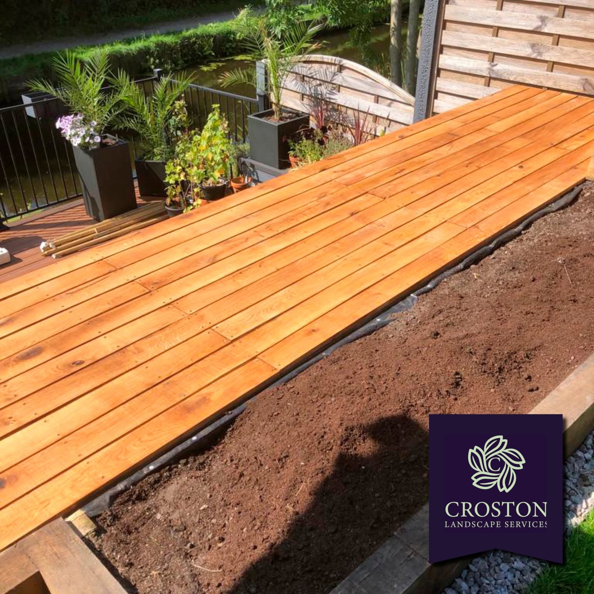Long cedar deck walkway beside fresh borders and a canal-side garden