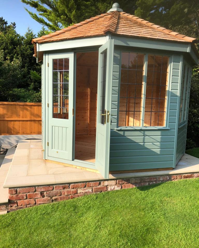 Sage-green summerhouse with cedar shingle roof, doors open, on a raised brick plinth