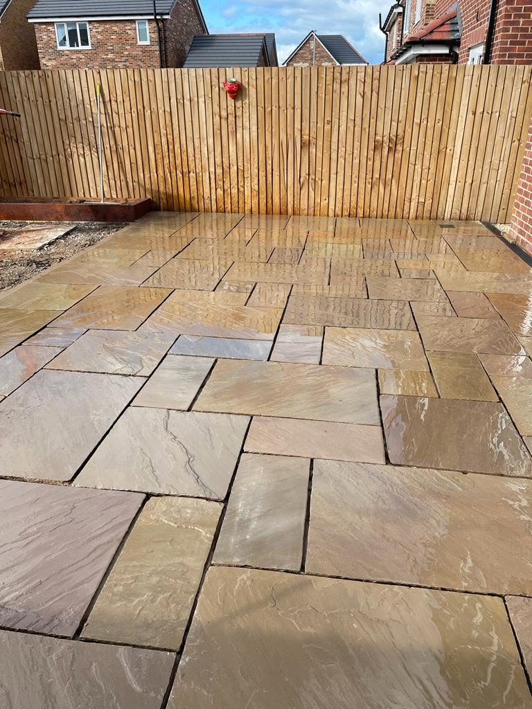 Indian sandstone patio laid against a tall timber fence, freshly sealed
