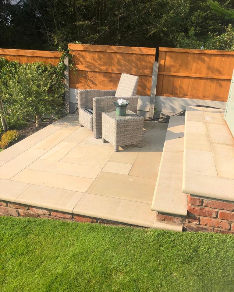 Raised sandstone patio with brick plinth, rattan furniture on the lawn