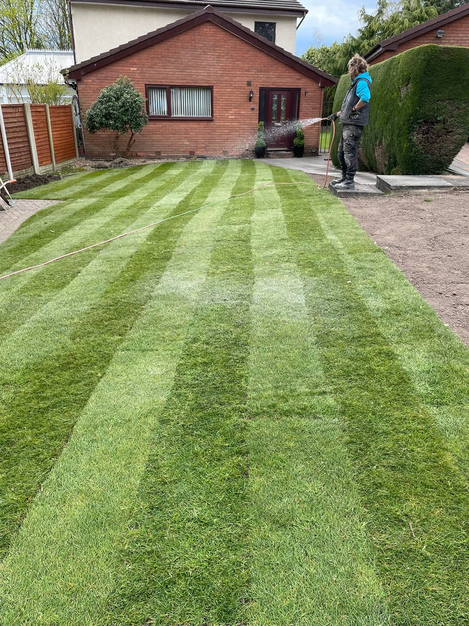 Team member hosing down a freshly laid perfectly striped turf lawn